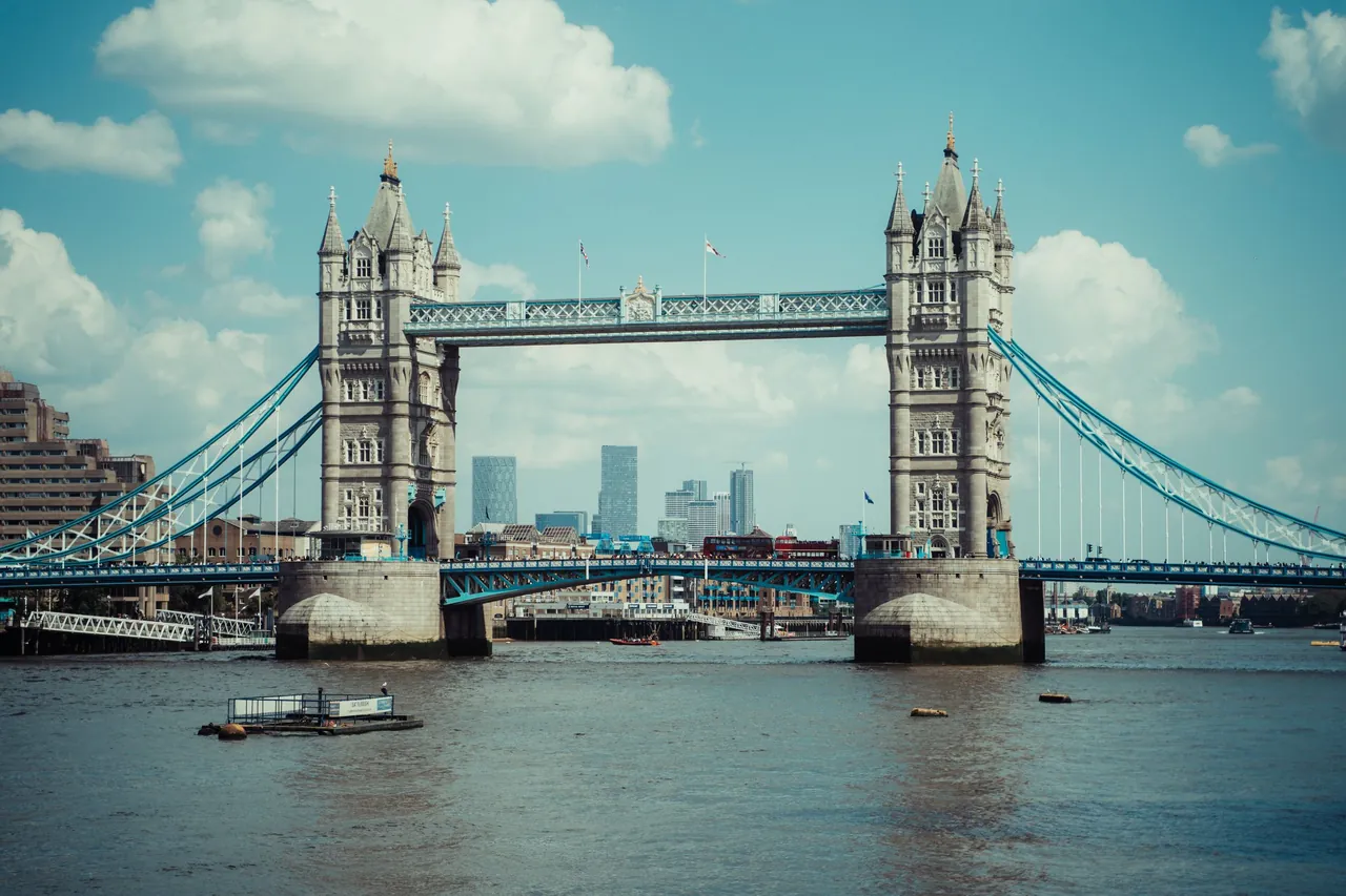 Tower Bridge over the Thames with the towers of Canary Wharf behind, under a bright sky